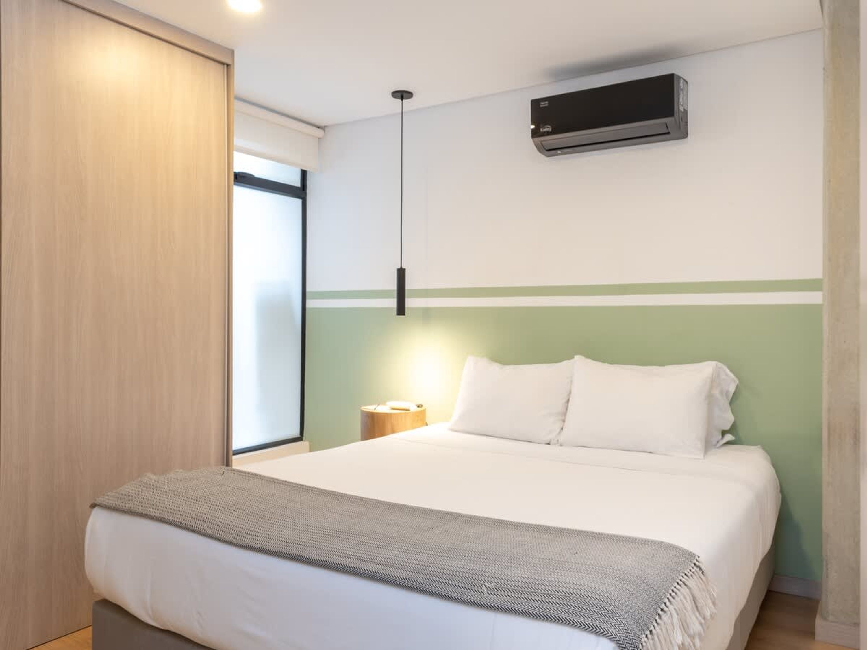 Une chambre à coucher comprenant un lit, une table de chevet, une lampe, un appareil de climatisation et une fenêtre donnant sur un paysage agréable.