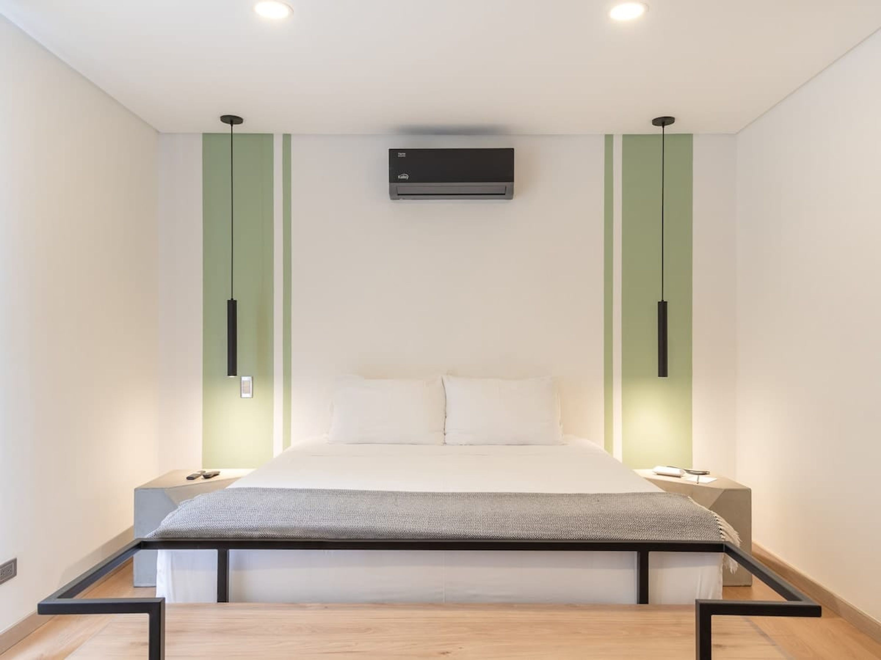 A modern bedroom with a bed, green cabinets, and a ceiling-mounted air conditioner.