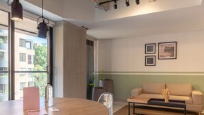 Ein modernes Wohnzimmer mit einem Holzespeisetisch, einer Couch und einem Couchtisch. An der Wand hängen gerahmte Bilder und es steht eine Pflanze in einem Topf.