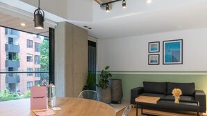 A modern living room with a round wooden table, a black sofa, and a large window offering a view of a building and greenery. - Cozy 3 BR w Balcony in Laureles Medell n (Medellín)