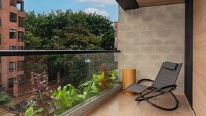 A balcony with a glass railing, a black lounge chair, and a view of greenery and buildings. - Cozy 3 BR w Balcony in Laureles Medell n (Medellín)