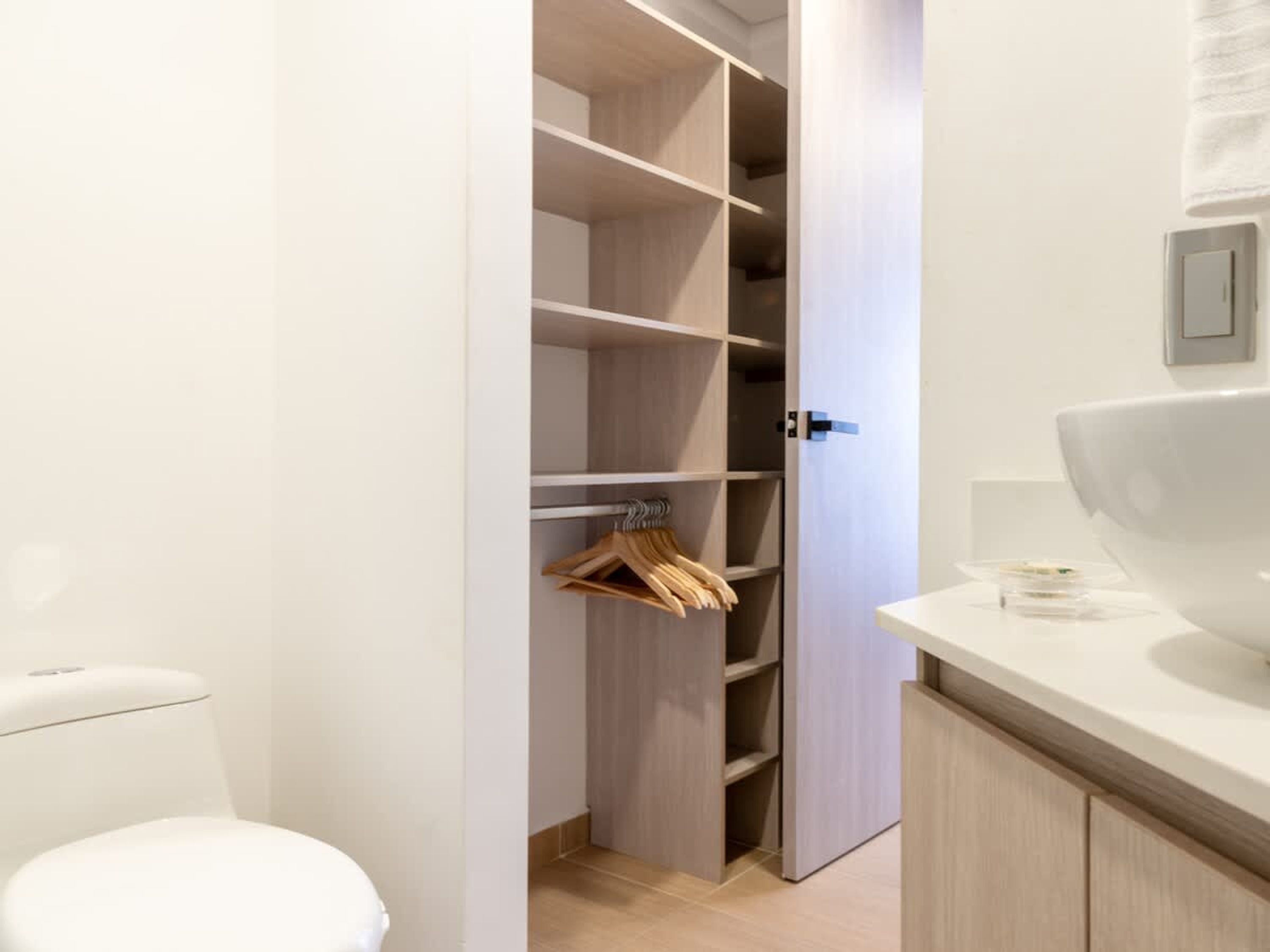 Un baño moderno con inodoro, lavamanos blanco y tocador de madera.