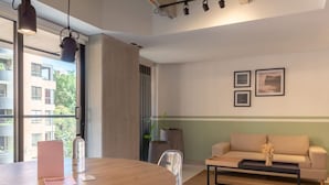 A modern living room with a wooden dining table, a sofa, and a coffee table. There are two framed pictures on the wall and a potted plant. - Stylish 3BR in Laureles MDE (Medellín)