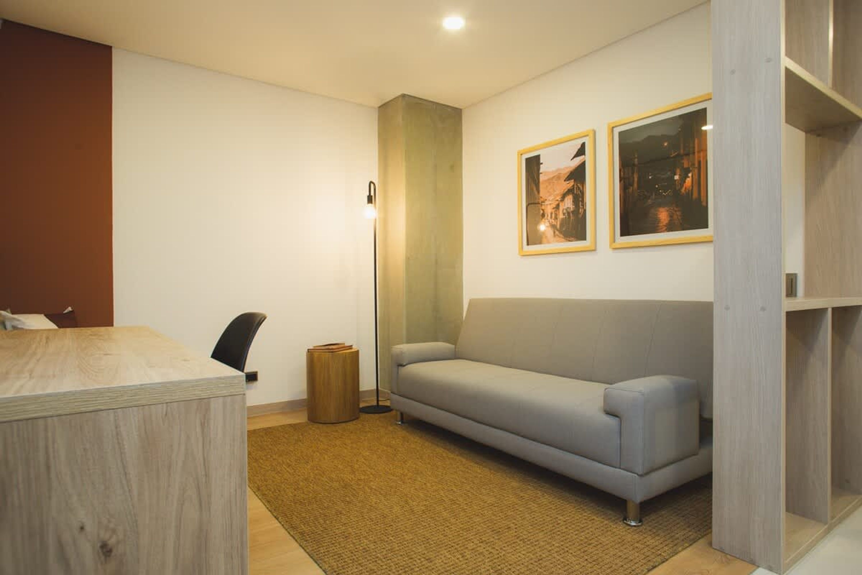 A modern room with a wooden desk, a grey sofa, a small trash bin, and two framed pictures on the wall.