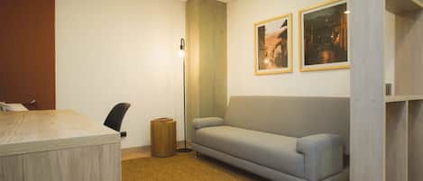 A modern room with a wooden desk, a grey sofa, a small trash bin, and two framed pictures on the wall.