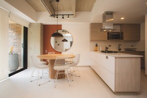 A modern kitchen with a central island, white chairs, and a round mirror on the wall. - Cozy 3 BR in Laureles in Medell n (Medellín)