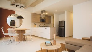 A modern kitchen with white cabinetry, a central island, and a black refrigerator. There is a dining area with white chairs and a small round table. - Cozy 3 BR in Laureles in Medell n (Medellín)