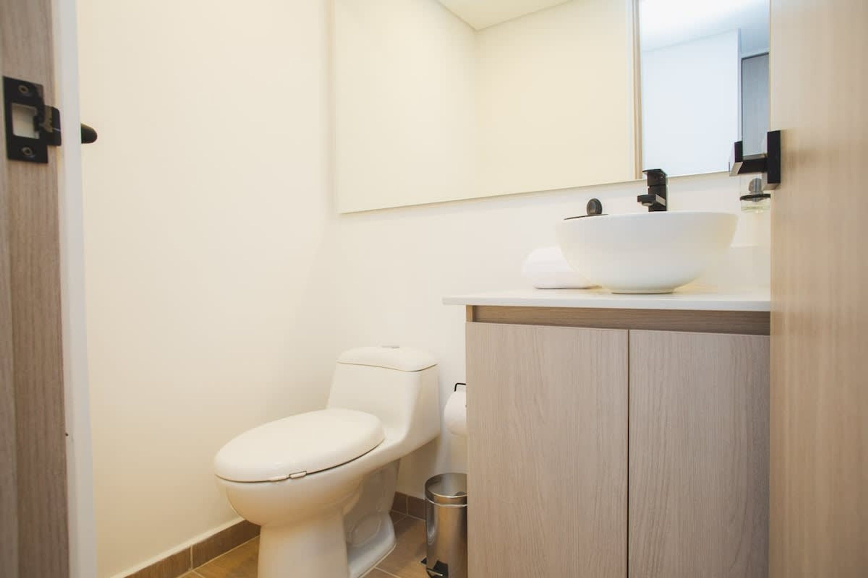 A modern bathroom with a white toilet, a sink with a vessel basin, and a mirror above the sink.