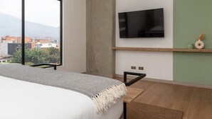A modern bedroom with a large window, a bed, a mounted TV, and a small shelf with decorative items. - Beautiful 3BR in Laureles Medell n (Medellín)
