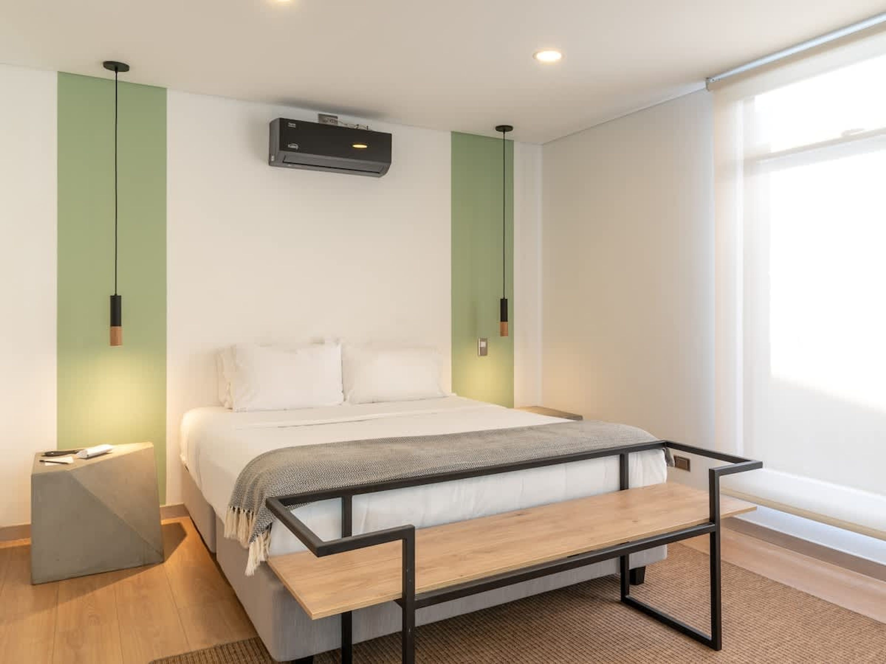 Un dormitorio moderno con cama, mesitas de noche, un banco y aire acondicionado instalado en la pared.