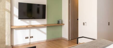 Una habitación moderna con televisión montada, estante de madera, puerta y alfombra estampada.