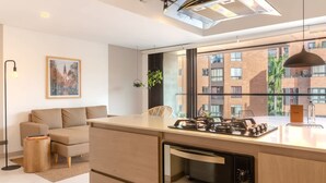 A modern kitchen with a built-in oven, a dining area with a sofa, and a large window offering a view of a brick building.