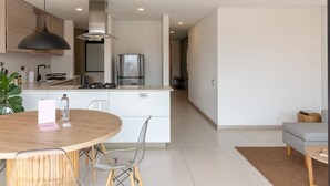 Eine moderne Küche mit einer zentralen Kochinsel, ein Essbereich mit rundem Tisch und Stühlen sowie eine Wohnbereits mit einer Couch und einem Couchtisch.
