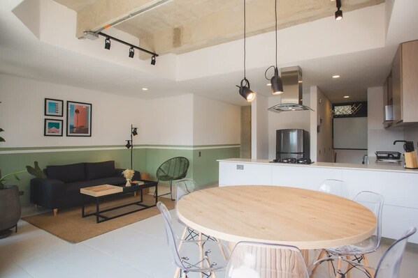 A modern kitchen with a central island, a dining area with a round table, and a living space with a sofa and chairs.
