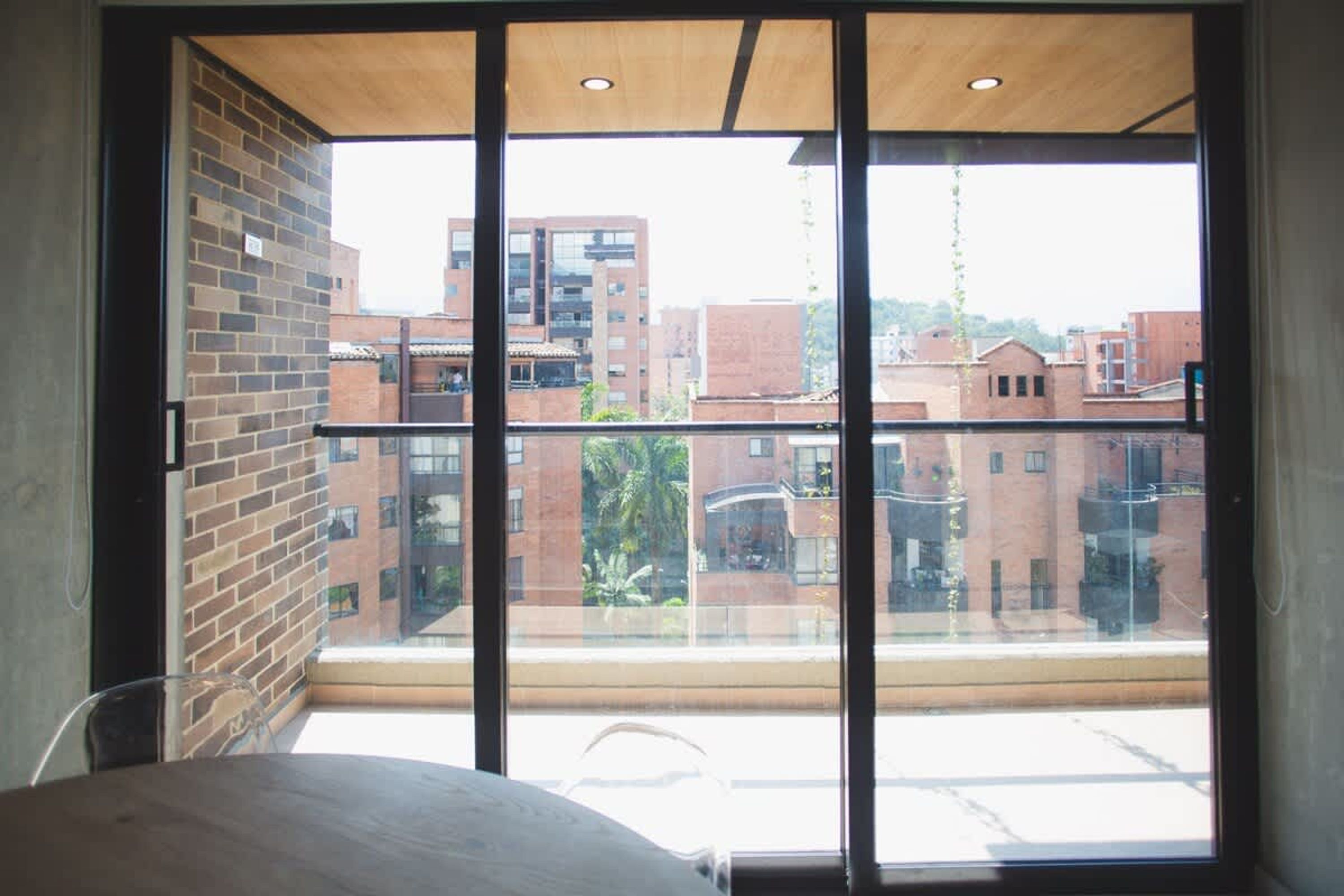 Una habitación con un ventanal grande, una pared de ladrillo y vistas de edificios circundantes.