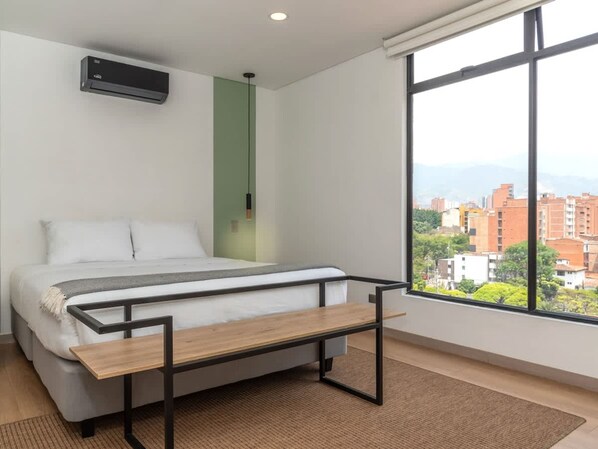 Un dormitorio moderno con cama, mesita de noche, ventana con vistas a la ciudad y aire acondicionado.