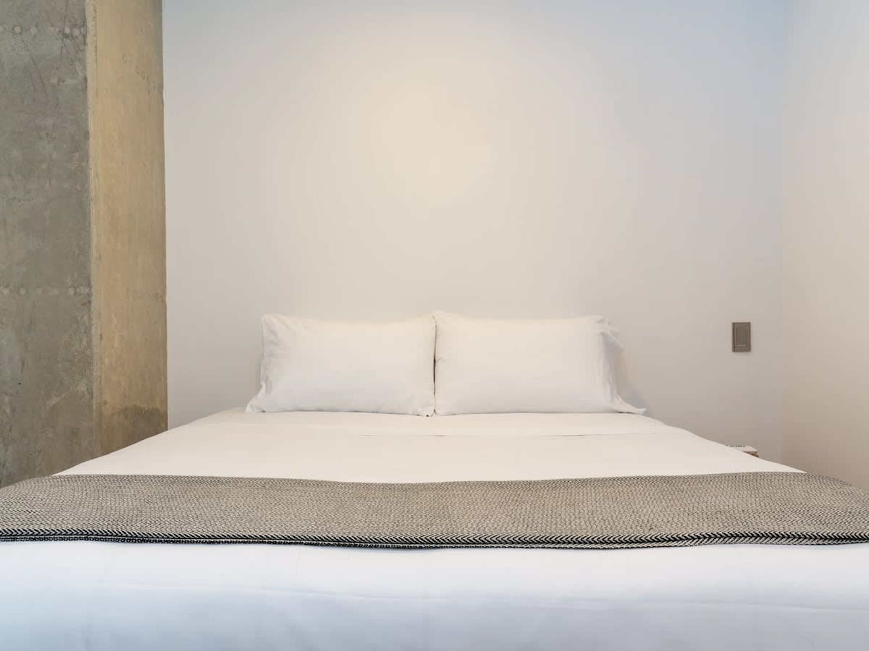 A minimalist bedroom with a bed, two pillows, and a textured throw blanket.