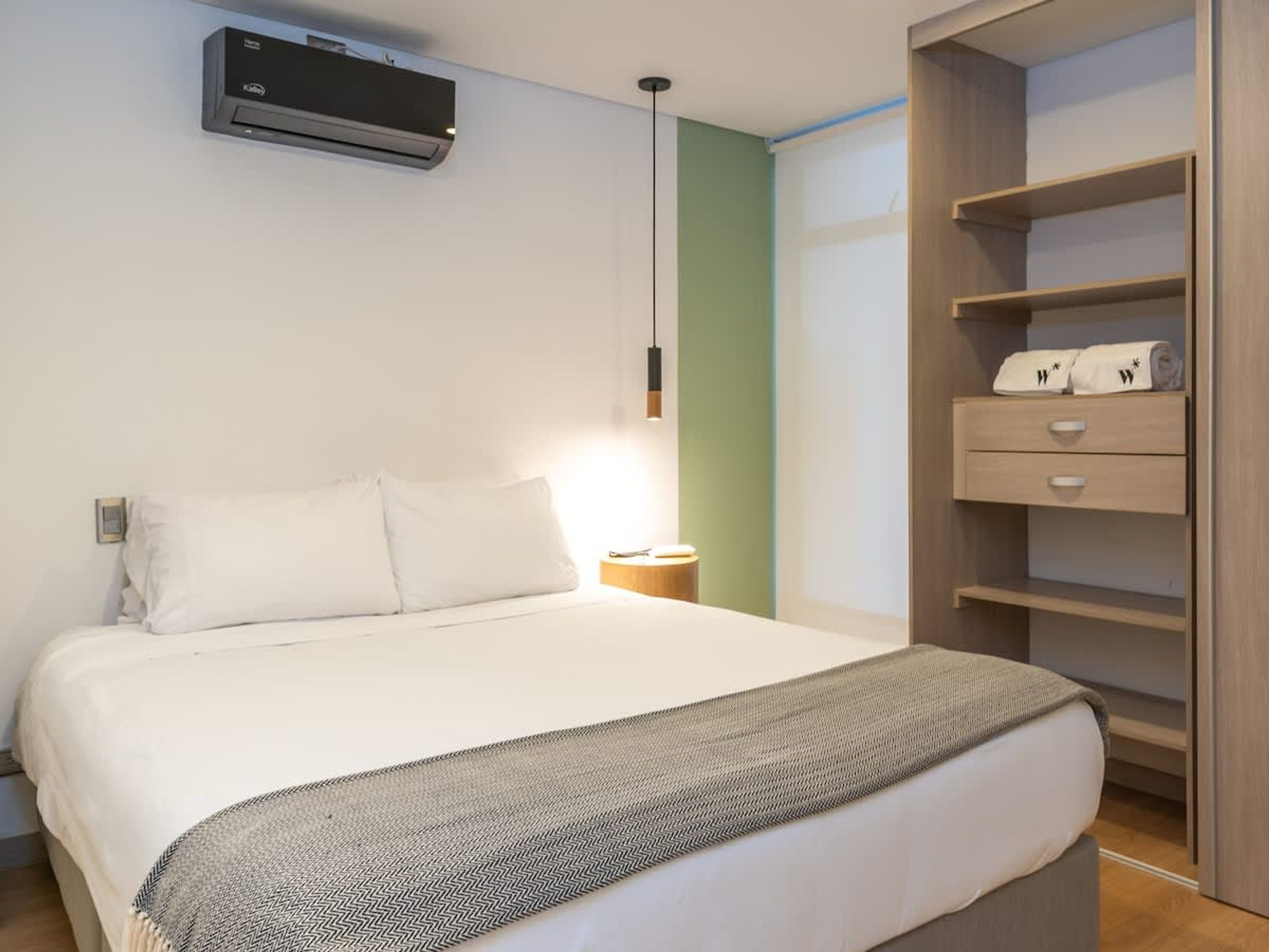 Quarto com cama, mesa de cabeceira, guarda-roupa e ar condicionado.