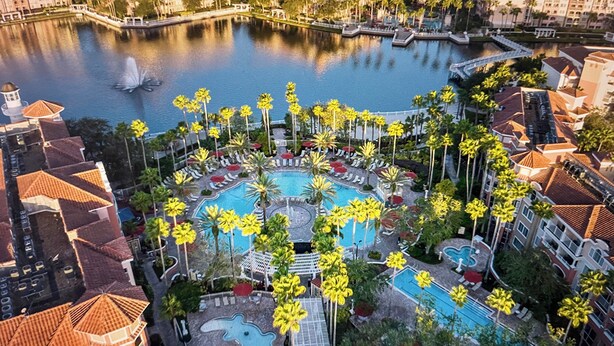 Vista aérea de un resort con varias piscinas, palmeras y una gran extensión de agua.