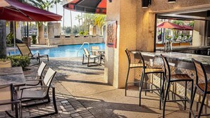 Zona de piscina exterior con sillones reclinables y un bar.