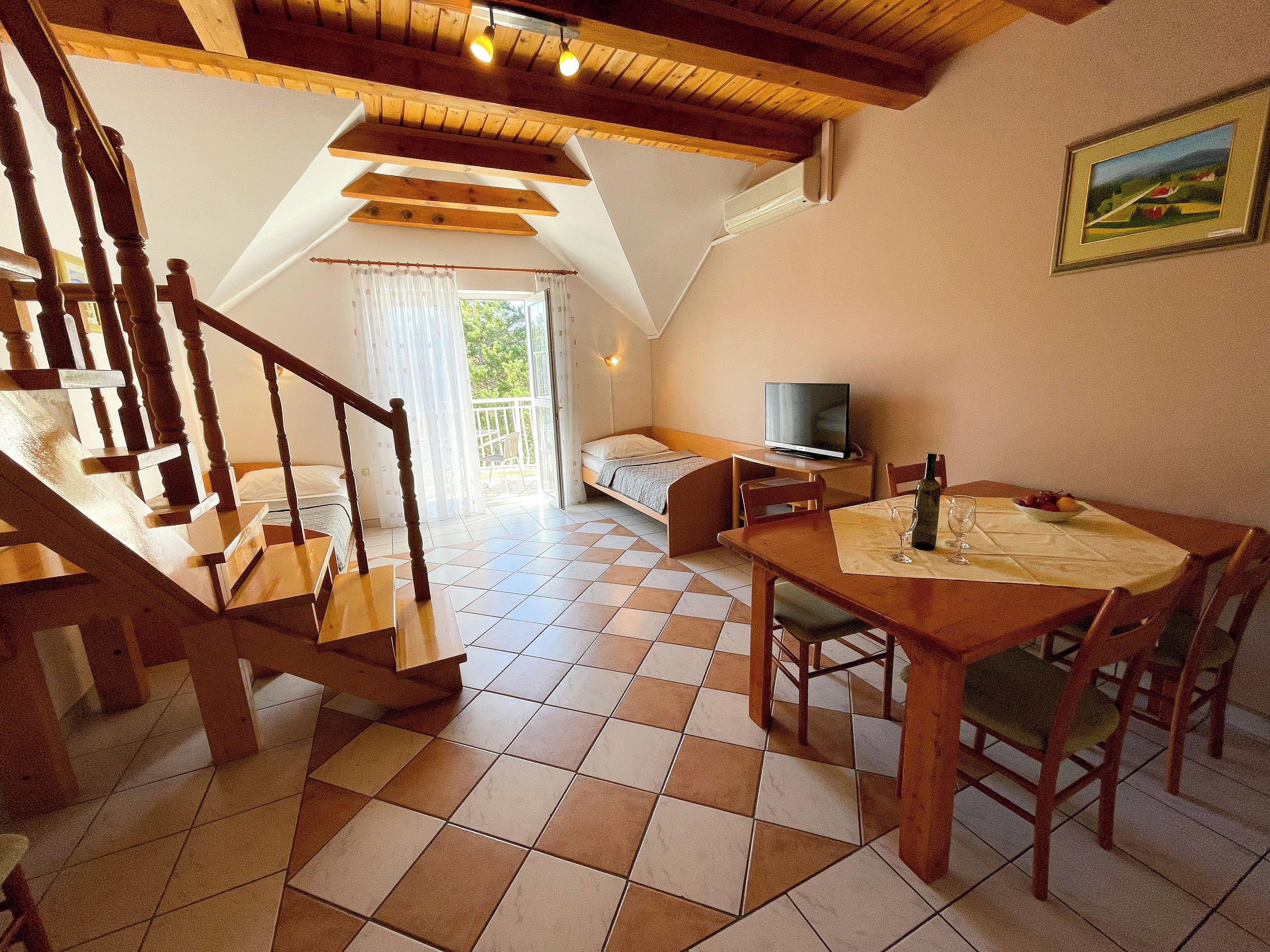 A cozy room with a wooden staircase, a bed, a TV, and a dining table with chairs.