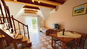 Ein gemütliches Zimmer mit einer Holztreppe, einem Bett, einem Fernseher und einem Esstisch mit Stühlen.