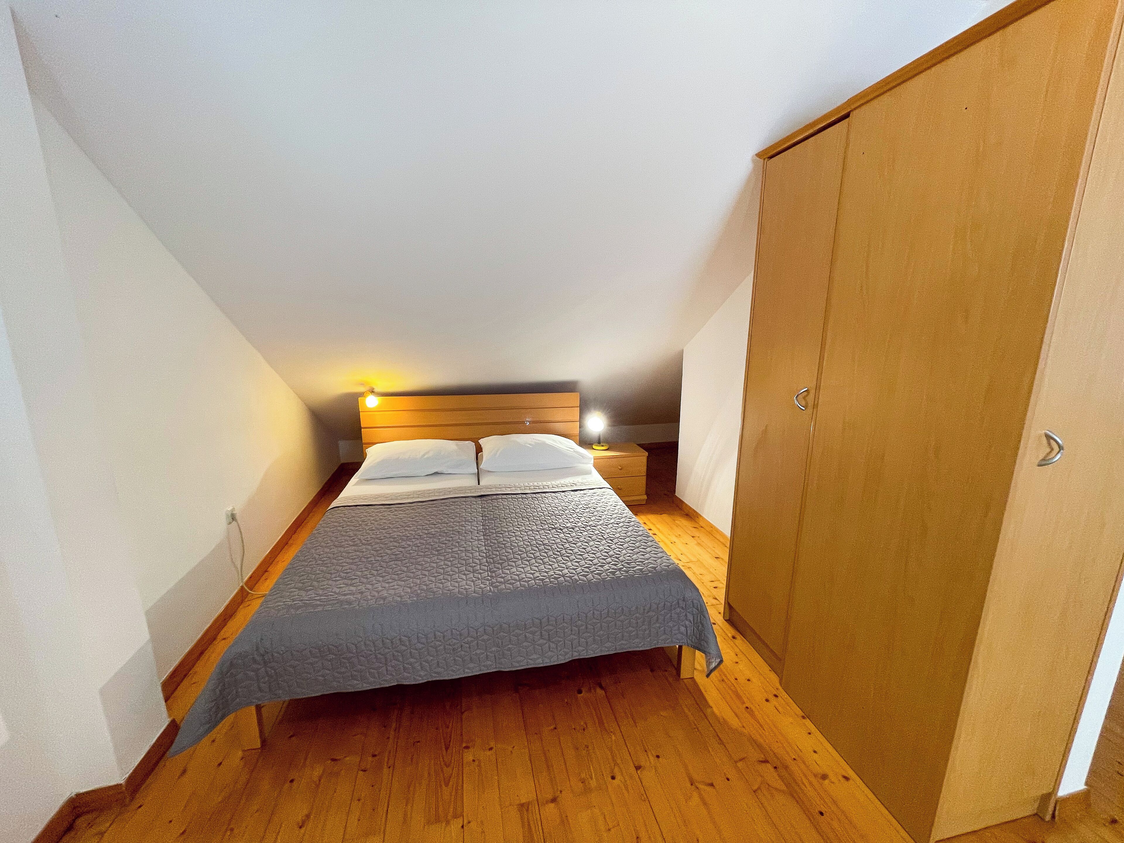 Une petite chambre à coucher, chaleureuse et accueillante, avec un lit simple, une armoire en bois et un plafond en pente.