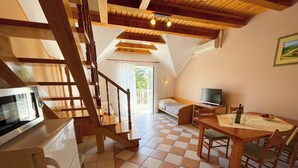 Ein gemütliches Zimmer mit Esstisch, Stühlen, einem Fernseher und einer Treppe, die auf einen Balkon führt.