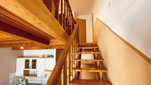 Eine Holztreppe führt zu einer oberen Etage, darunter ist eine Küche zu sehen.