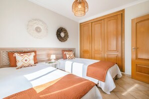 A hotel room with two beds, a wooden wardrobe, a round wall decoration, and a hanging light fixture. - Our House in Clube Albufeira (Albufeira)