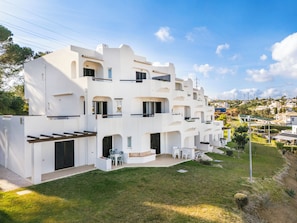 A modern multi-story residential building with balconies, a small patio area with outdoor seating, and a well-maintained lawn. - Our House in Clube Albufeira (Albufeira)