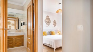 Une chambre d’hôtel comprenant un lit, une table de chevet, une lampe, des éléments décoratifs sur les murs, ainsi qu’une salle de bain avec un lavabo, un miroir et des placards.