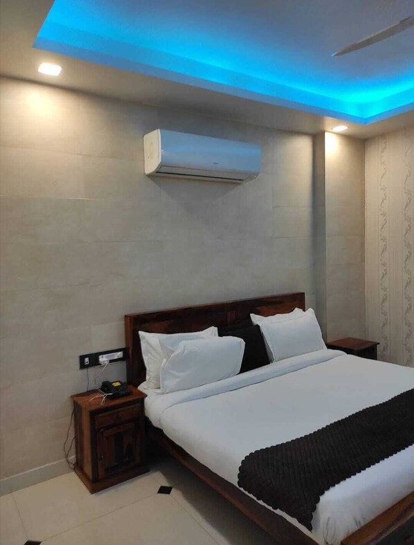 A modern hotel room with a large bed, bedside tables, an air conditioning unit, and a ceiling with blue lighting.