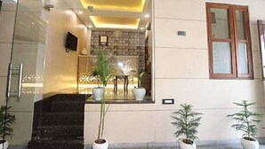A reception area with a glass partition, a staircase, and potted plants. - LAVIT HOTEL (Faridabad)