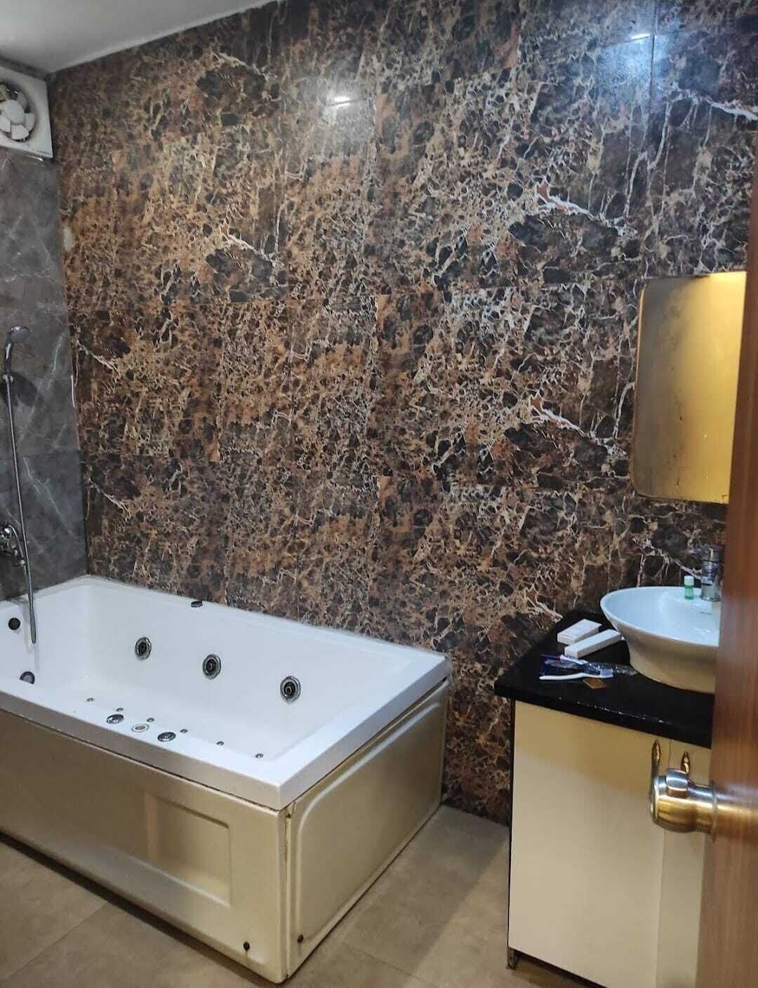 A bathroom with a marble wall, a bathtub, a sink, and a mirror.
