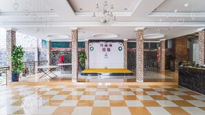 Tilava aula, jossa on ruutukuviollinen lattia, vastaanottotiski ja suuri kattokruunu.