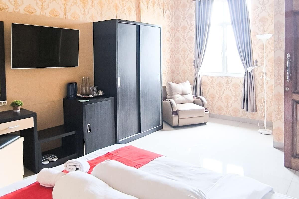 A hotel room with a bed, a TV, a wardrobe, a chair, and a window with curtains.