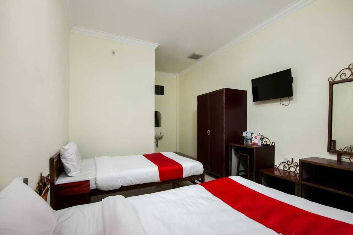 A hotel room with two beds, a TV, a wardrobe, and a desk.