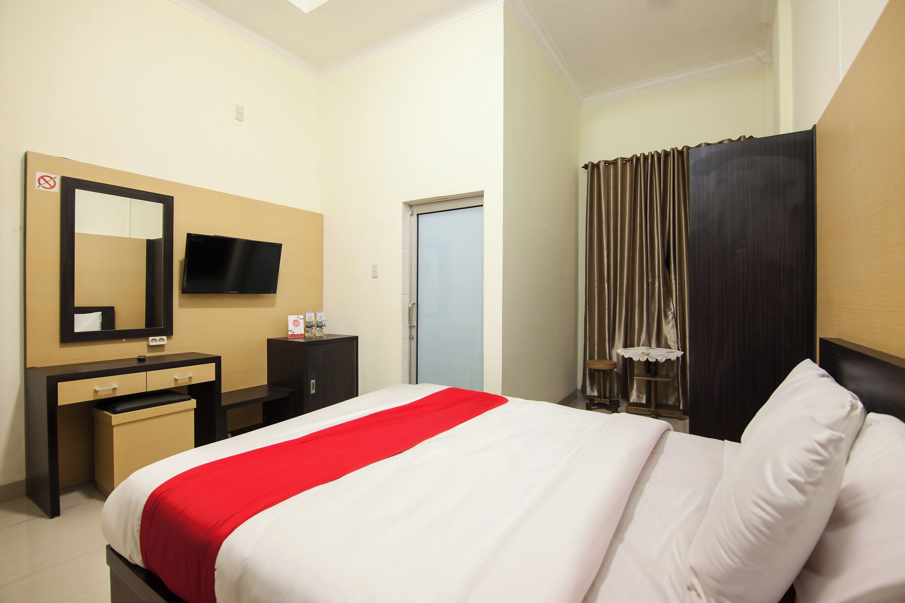Une chambre d’hôtel avec un lit, un bureau avec un miroir, une télévision et une porte.