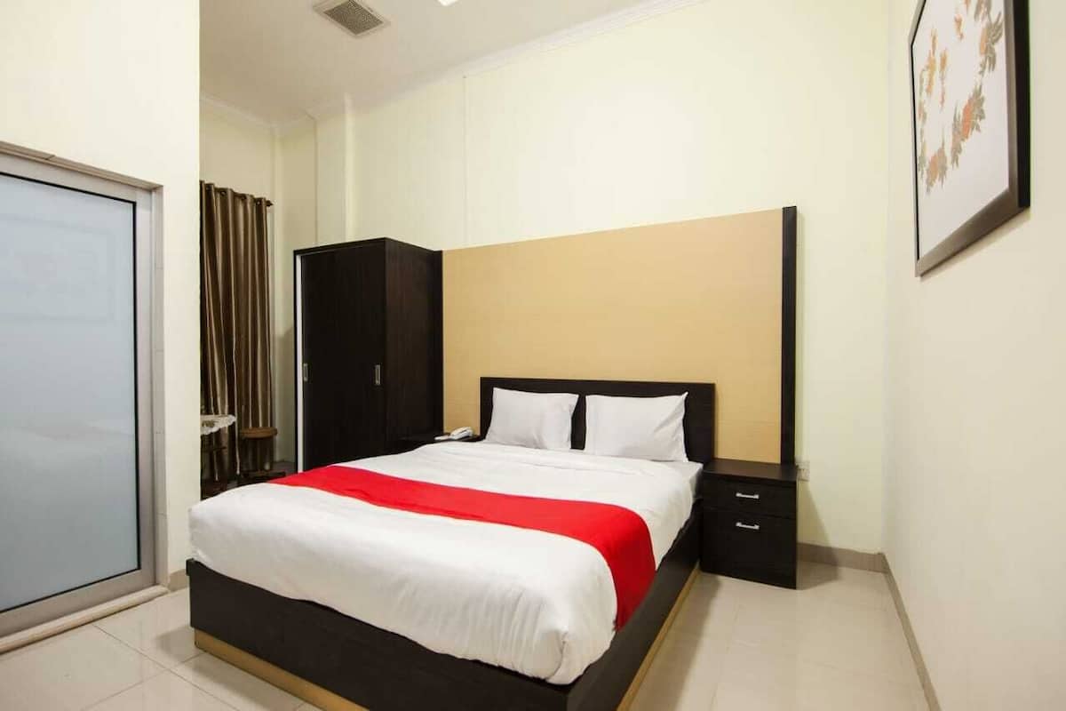 A hotel room with a bed, a wardrobe, a bedside table, and a door.