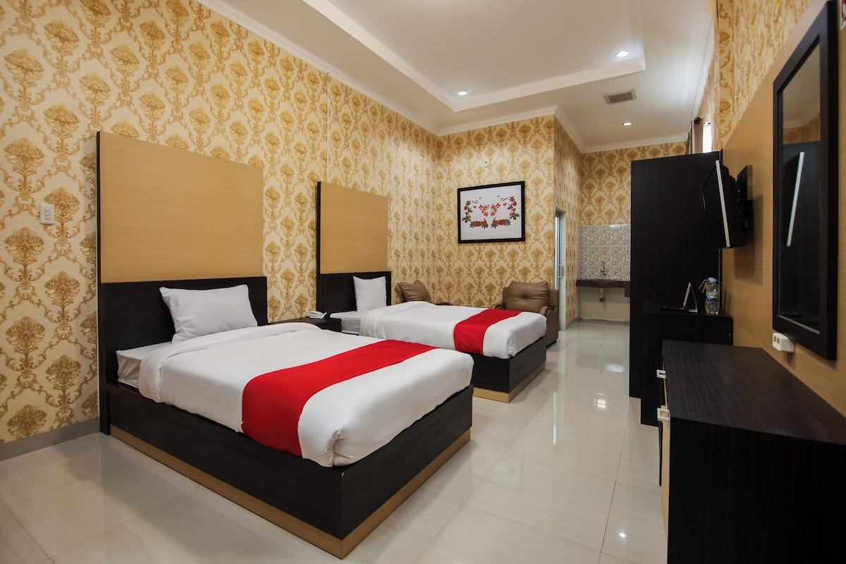 A hotel room with two beds, a TV, and a bathroom visible in the background.