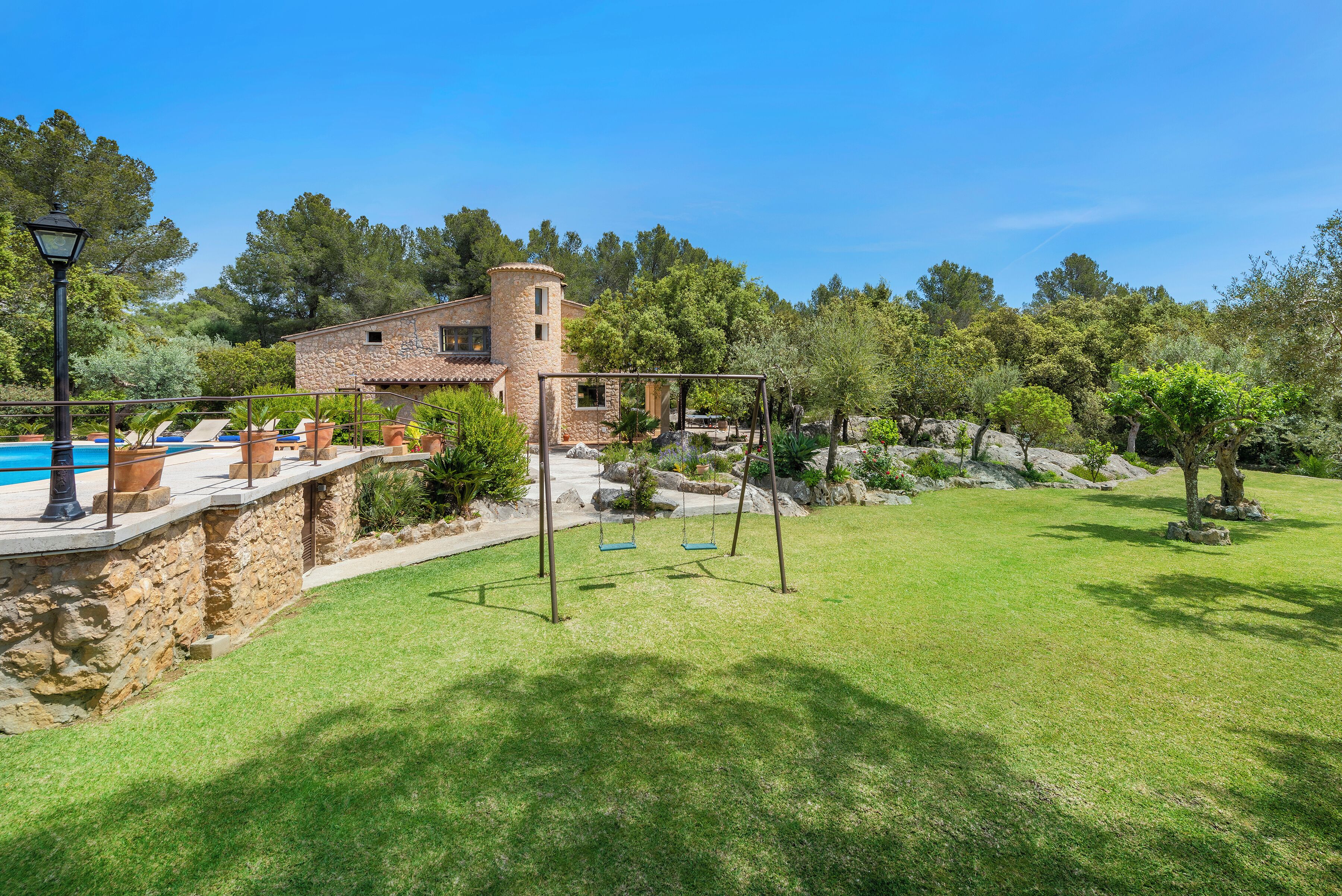 Une maison en pierre avec une piscine, une balançoire et une pelouse bien entretenue.