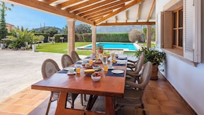 Un porche cubierto con una mesa de madera dispuesta para el desayuno, con vista a una piscina.
