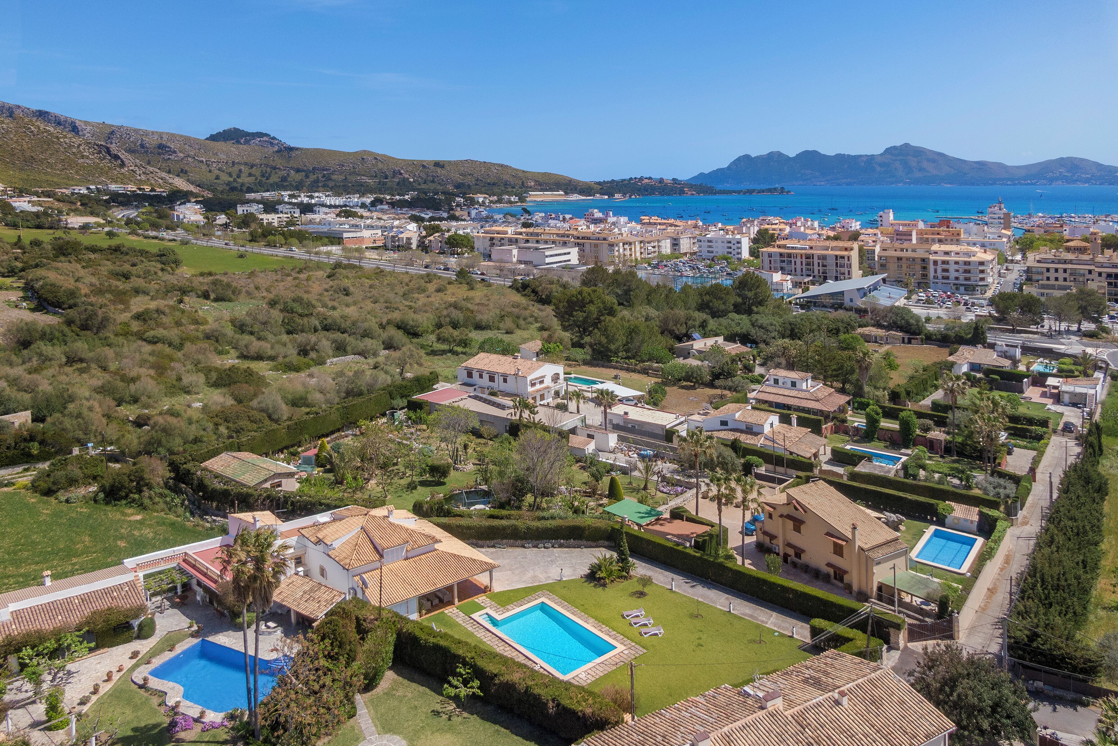 Ett flygbildsfoto av ett bostadsområde vid kusten med flera byggnader, en swimmingpool och en fri utsikt över havet.