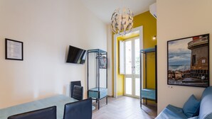 A room with a dining table, chairs, a TV mounted on the wall, a hanging light fixture, and a framed picture on the wall. - Central Station Housing Apartments (NAPOLI)