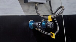 A water heater mounted on a tiled wall with a control panel and hoses. - Freetown Resort-Gulu (Gulu)