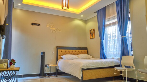 A neatly arranged bedroom with a bed, bedside table, chair, and a wall-mounted sign. - Freetown Resort-Gulu (Gulu)