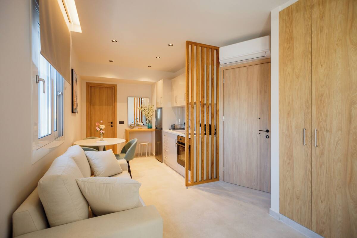 A modern kitchen with wooden cabinets, a dining area with a table and chairs, and a sofa in a living area.