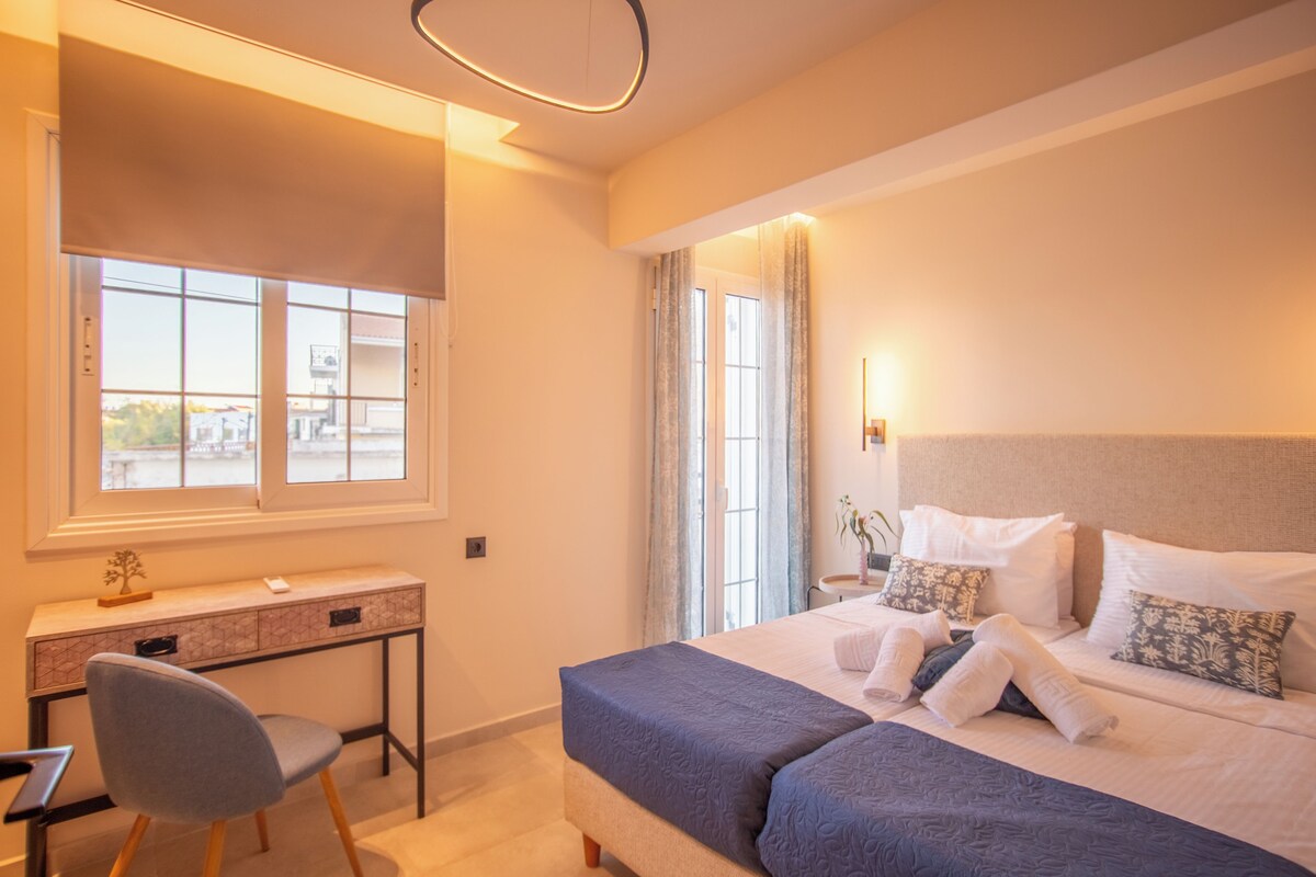 Un dormitorio con cama, mesita de noche, silla y ventana con cortinas.