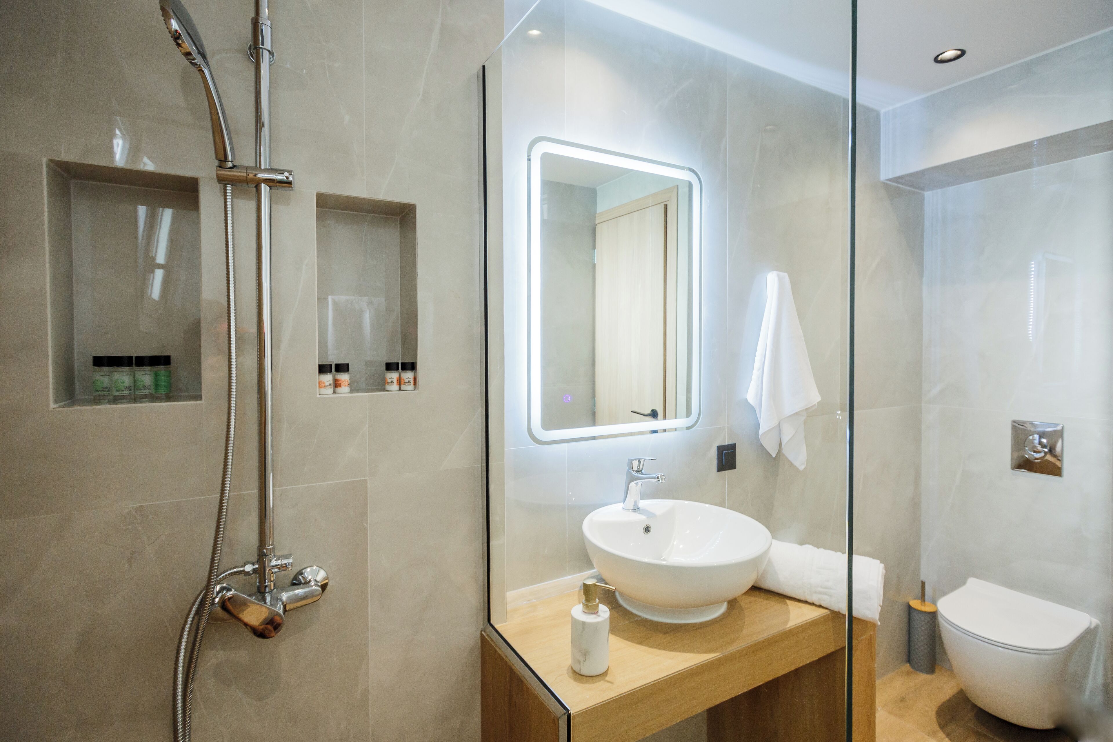 A modern bathroom with a glass-enclosed shower, a wooden vanity with a white sink, and a large mirror with built-in lighting.